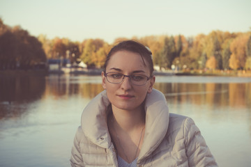 Осенний портрет девушки в очках на фоне водоема