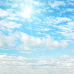 Sun on blue sky with white clouds.