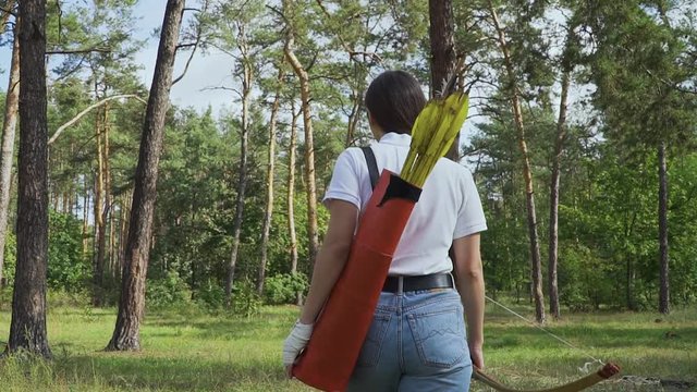 Beautiful girl with a bow and arrows goes through the forest
