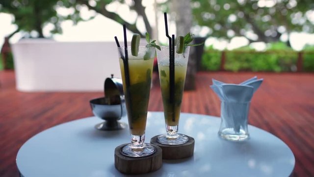 Focus pull from bowl bar snacks onto cocktail glasses in foreground garnished with fresh mint, luxurious private resort restaurant patio. Slow motion 50p.