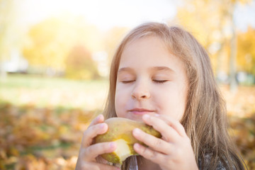 Portrait of a beautiful little girl who eats a pear on a picnic in the autumn park