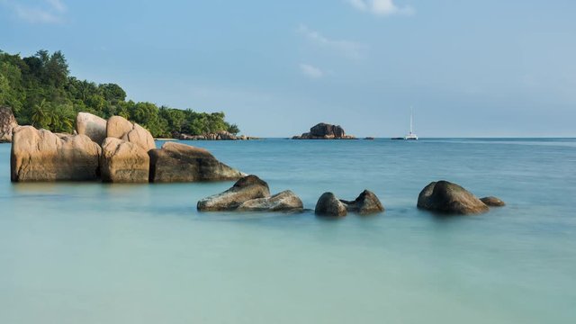 Timelapse of calm scenic late afternoon (golden) beach and waves at Anse st. Sauveur on Praslin Island, with granitic rock boulders, catamaran (yacht). 4K, 25p.