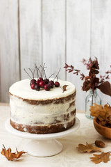 Apple cake with cream, decorated with small apples against the background of autumn composition. Rustic style.