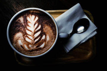 Latte art for white leaf, cup of hot coffee on wooden plate in dark tone