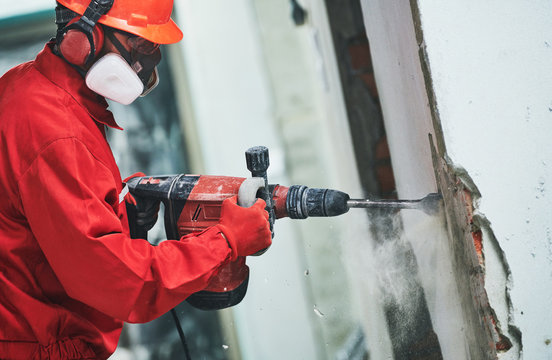 worker with demolition hammer removing plaster or stucco from wall
