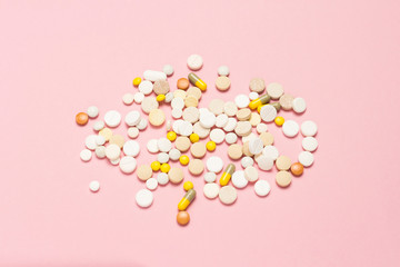 Pills of different sizes and colors on a light pink background.