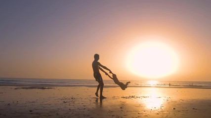 Silhouette of father playing with his son making him flying in the beach at sunset