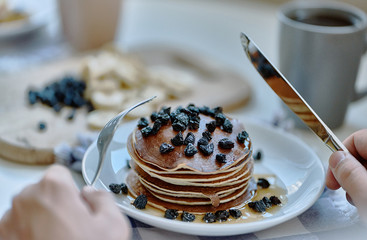 Man eats with a fork and knife pancakes with berries.