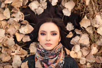 Autumn consept. Portrait of an autumn woman lying over leaves outside in fall forest. Beautiful mixed race Caucasian Asian young girl.