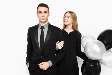 beautiful stylish couple, young girl in a black dress and a man in a black suit, holding balloons and bags, for shopping, on a white background. Black Friday