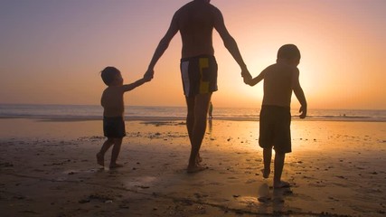 Silhouette of father with two children in the beach at sunset