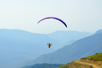 Skydiver flying on colorful parachute in blue sky over mountains in summer day