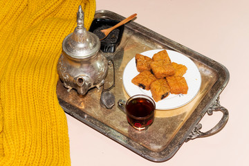arabic breakfast with winter scarf, algerian cookies named makrout on white plate and a tea cup, silver antique teapot