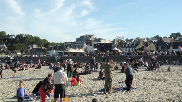 [EDITORIAL] BINIC, FRANCE - JULY 31 2015: Vacationers on the beach in a summer evening with a stage in the town in background for the Binic Folks Blues Festival. Many people, colorful 4k motion.