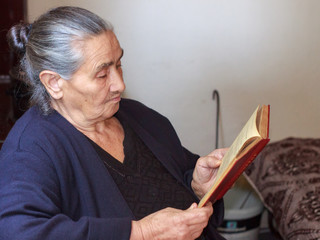 Old fashioned elder woman reading a book alone in the kitchen