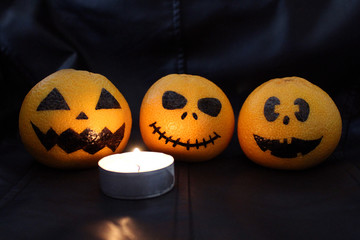 Halloween concept. Funny orange mandarins or tangerines pumpkin painted in the form of icons of Halloween on a black background. Painted scary faces on a holiday of halloween.