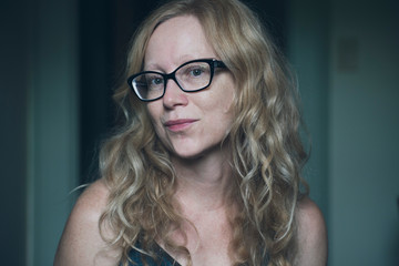 Woman with long reddish blonde wavy hair and wearing black frame glasses looks flirtatiously into...