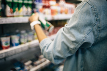 Female hand holding bottle yogurt near market shelves