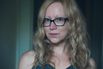 Woman with long reddish blonde wavy hair and wearing black frame glasses looks skeptically into the camera