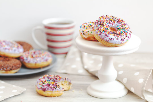 Delicious glazed donuts and cup of coffee on light wooden background
