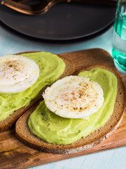 Rye bread avocado toasts with poached egg on wooden serving board. Brunch lunch meal