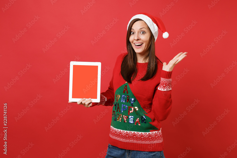 Wall mural surprised young santa girl spreading hands, holding tablet pc computer with blank empty screen isola