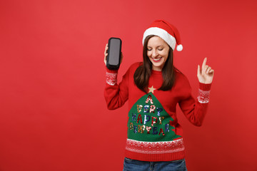 Relaxed young Santa girl dancing, looking down, pointing finger up, holding portable wireless...