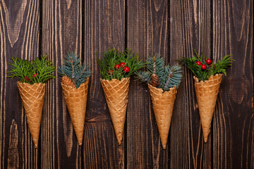 Christmas abstraction. A fir-tree  and thuja branch with cones and red berries  in waffle cups on dark wood, copy space