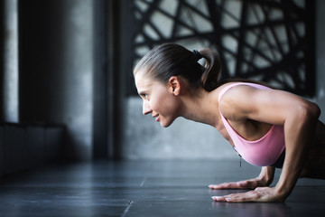 Athletic woman doing push-ups on the floor in a pink top.