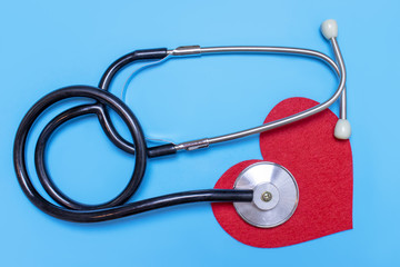 Red heart and a stethoscope on blue background, flat lay
