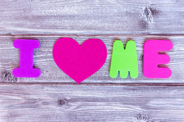 Sign i love me made of colorful letters and a heart on wooden background, self loving concept