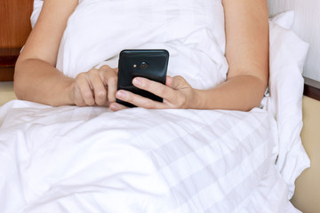 Cropped woman lying on bed. Pretty girl using cellphone and resting.