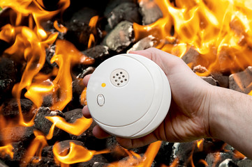 Rauchmelder in der Hand vor einem Feuerhintergrund