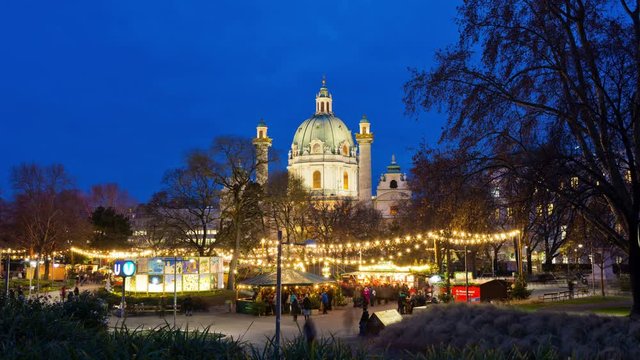 Popular Christkindlmarkt at fairy lights decorated Karlsplatz, time-lapse with crowd of people in festive mood in Christmas time in Vienna, Austria. Karlskirche (St. Charles's Church) in background.