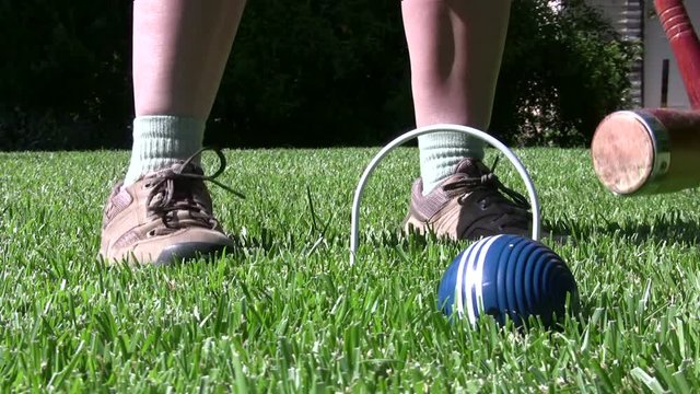 Close-up of feet of croquet player hitting shot through a wicket.
