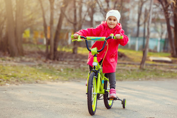 Little girl in red riding a bicycle outdoors