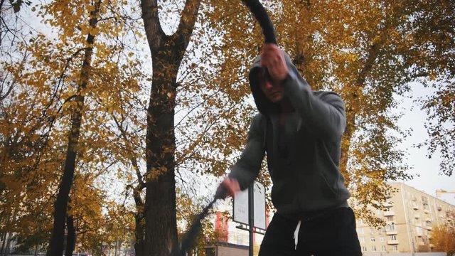 Young athlete in Hoodie trains with battle ropes in the autumn park