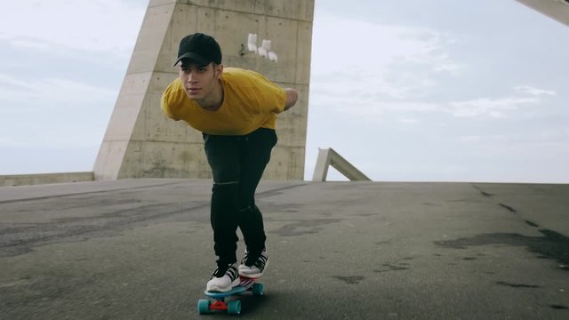Epic Portrait and close upt of a Young Attractive Trendy Man skateboarding fast under a solar panel on a morning sunny day with an urban city background in slow motion