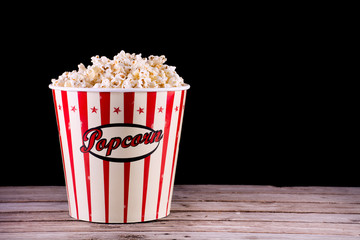 Popcorn in full retro box on wooden rustic desk and black background. Movie and cinema concept. Space for text and design