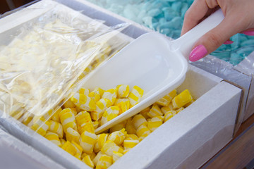 female hand with a scoop is picking up yellow candy from a cardboard box. details of candy at the candy shop
