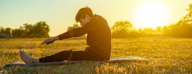 young man doing yoga asana outdoor at the sunset nature field  f