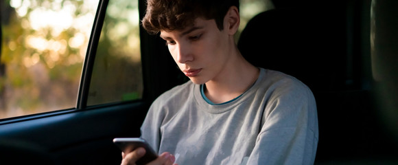 young male passenger sitting on car back seat using a smartphone а