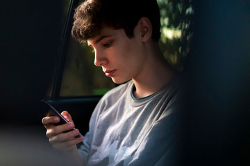 young male passenger sitting on car back seat using a smartphone а