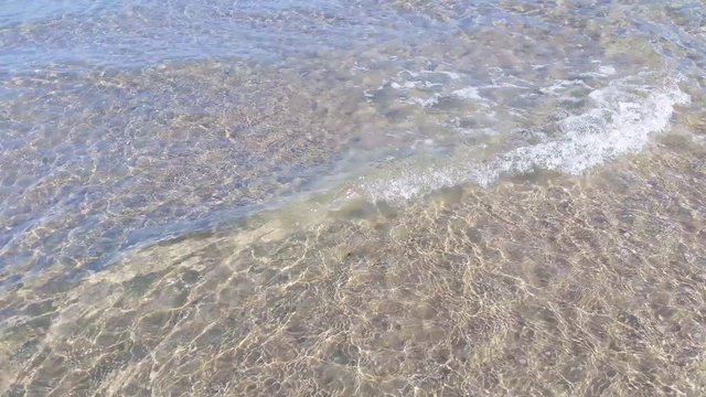 Pristine shallow and clear water, gentle waves, white foam and ripples. Ocean floor visible with sand ripples. Liseleje Beach by the Tisvilde forest and coastal area on the Danish island of Zealand.