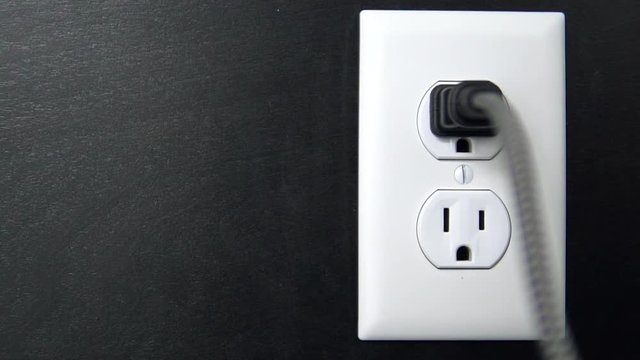 Male hand plugs in and unplugs a two pronged cord into the top outlet of an American electrical socket, copy space left