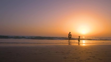 Silhouette of father with two children in the beach at sunset