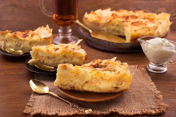 Portions of sweet dessert on plates, sour cream in a gravy boat, wooden background.