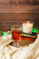 Cozy winter still life: cup of hot tea and books, candle on wooden background and blurred garland lights