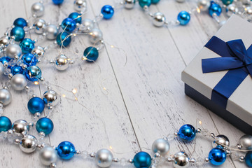 closeup Christmas gift with blue ribbon and silver and blue Christmas balls and garland on white wooden background