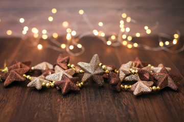 Christmas decoration in brown colors. Close up new year decor stars and bokeh garland on wooden background